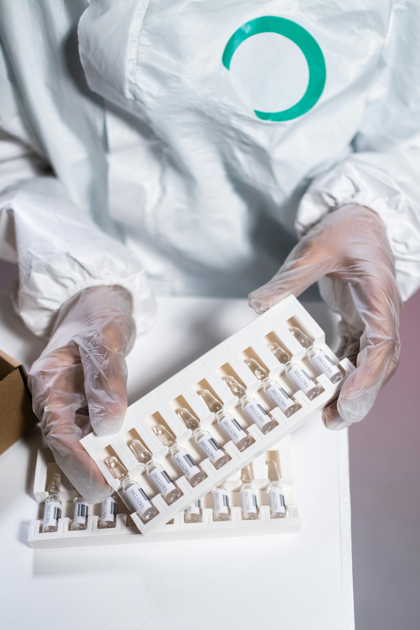 Healthcare worker in protective gear handling vials in a laboratory setting.